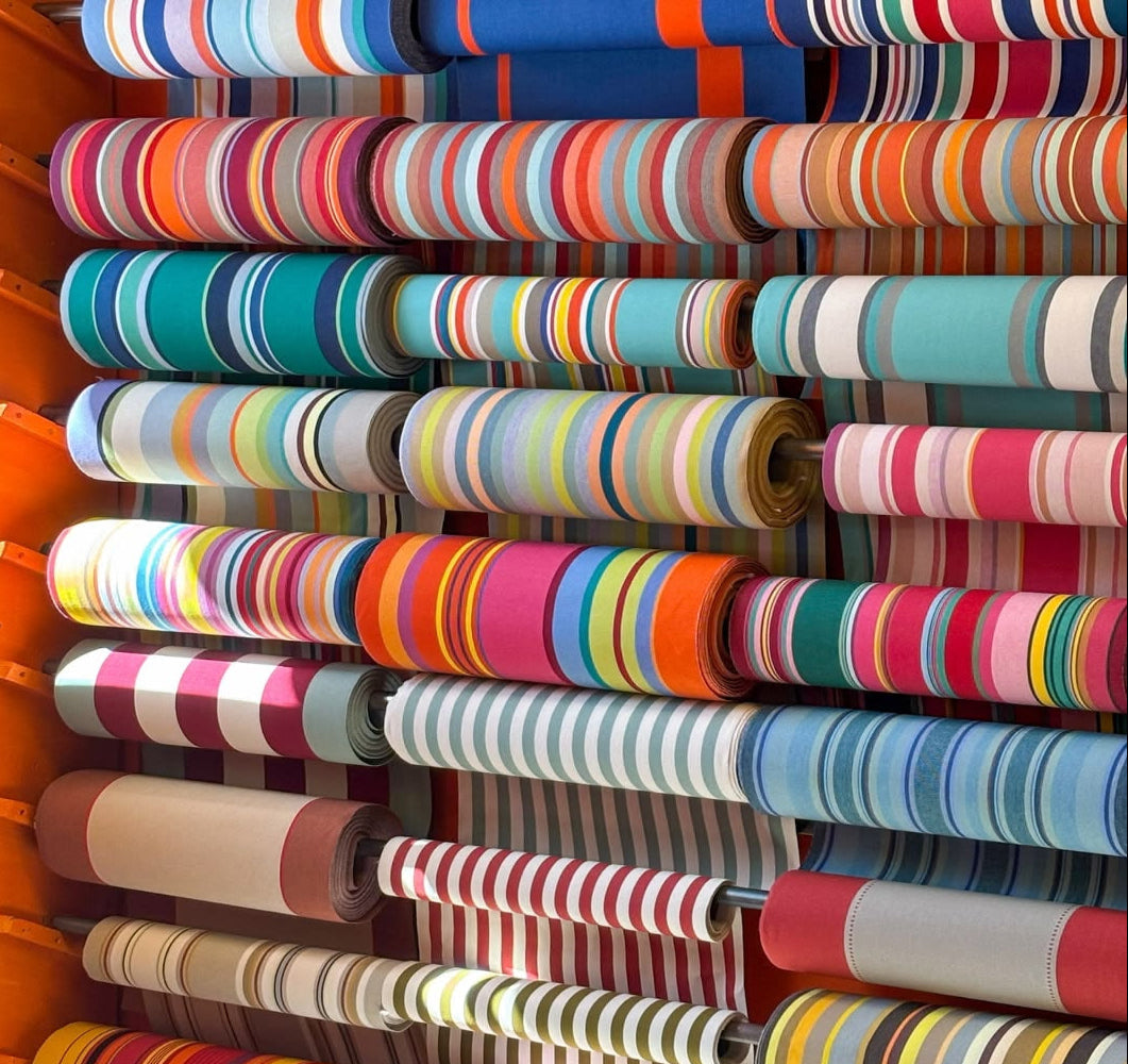 Multiple rolls of Les toiles du SOleil 100% woven colourful striped fabric stacked on a rack.