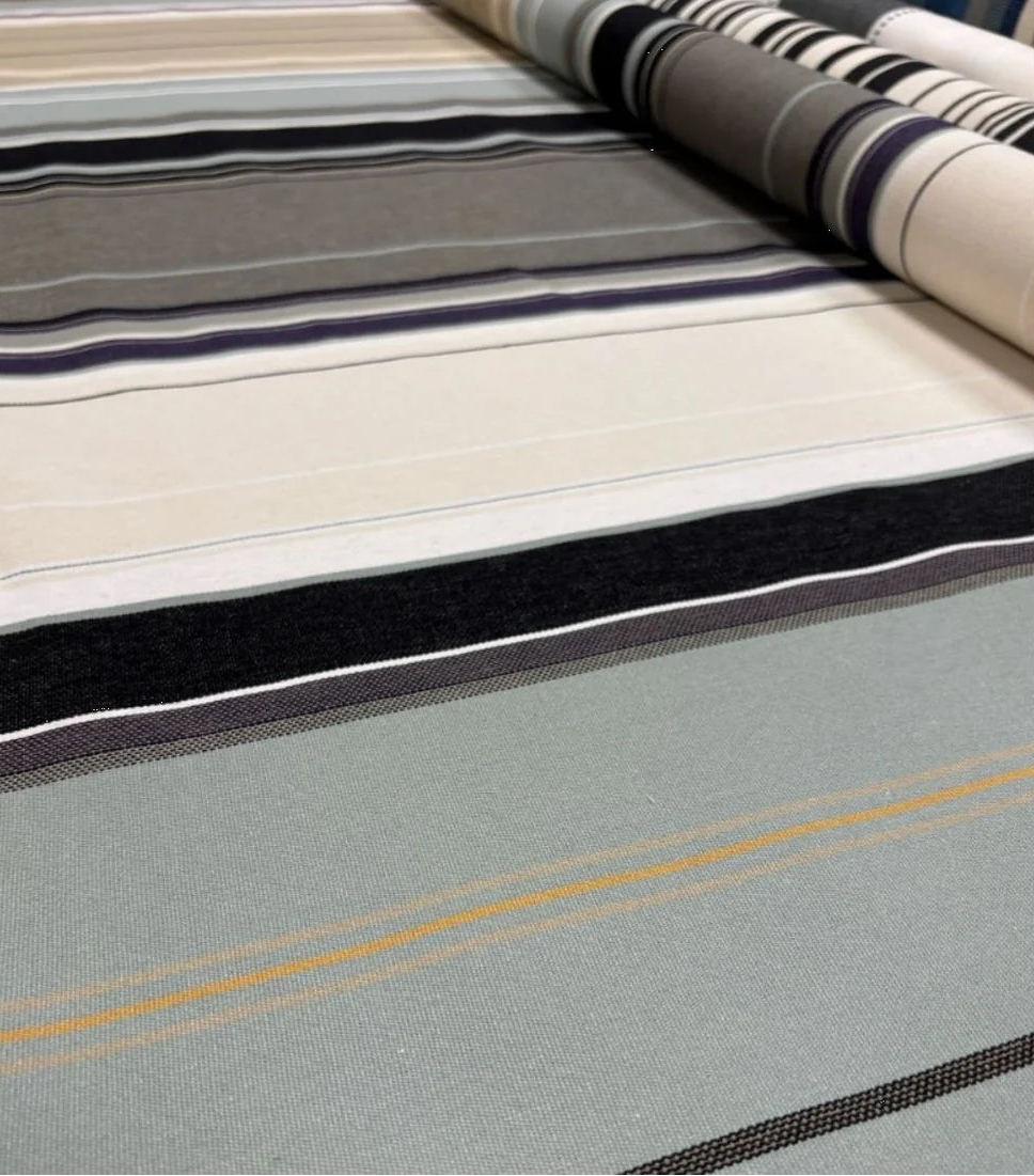 Close up of 100% cotton Les Toiles du Soleil fabric roll of Rue du Bac Gris - a multi striped woven pattern of different shades of greys, blues and beige