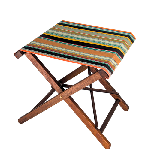 A folding wooden stool featuring densely woven stripes of orange, dark brown, golden yellow, teal, sand, olive, red and cream, with fine black and white pin lines throughout and bright orange selvedge edges.