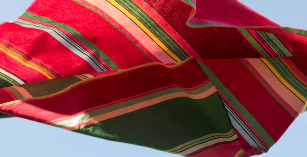 Red, yellow and green striped official Les Toiles du Soleil 100% cotton fabric against a clear blue sky