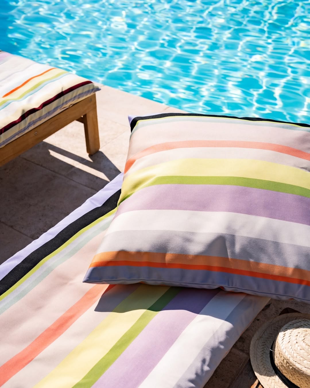 Colorful Les Toiles du Soleil St Colombe Outdoor Fabric striped cushions on lounge chairs by a poolside