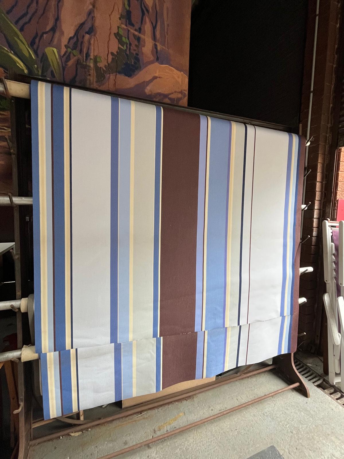Striped fabric  with blues, brown, lavender, and beige on a stand with a painting in the background