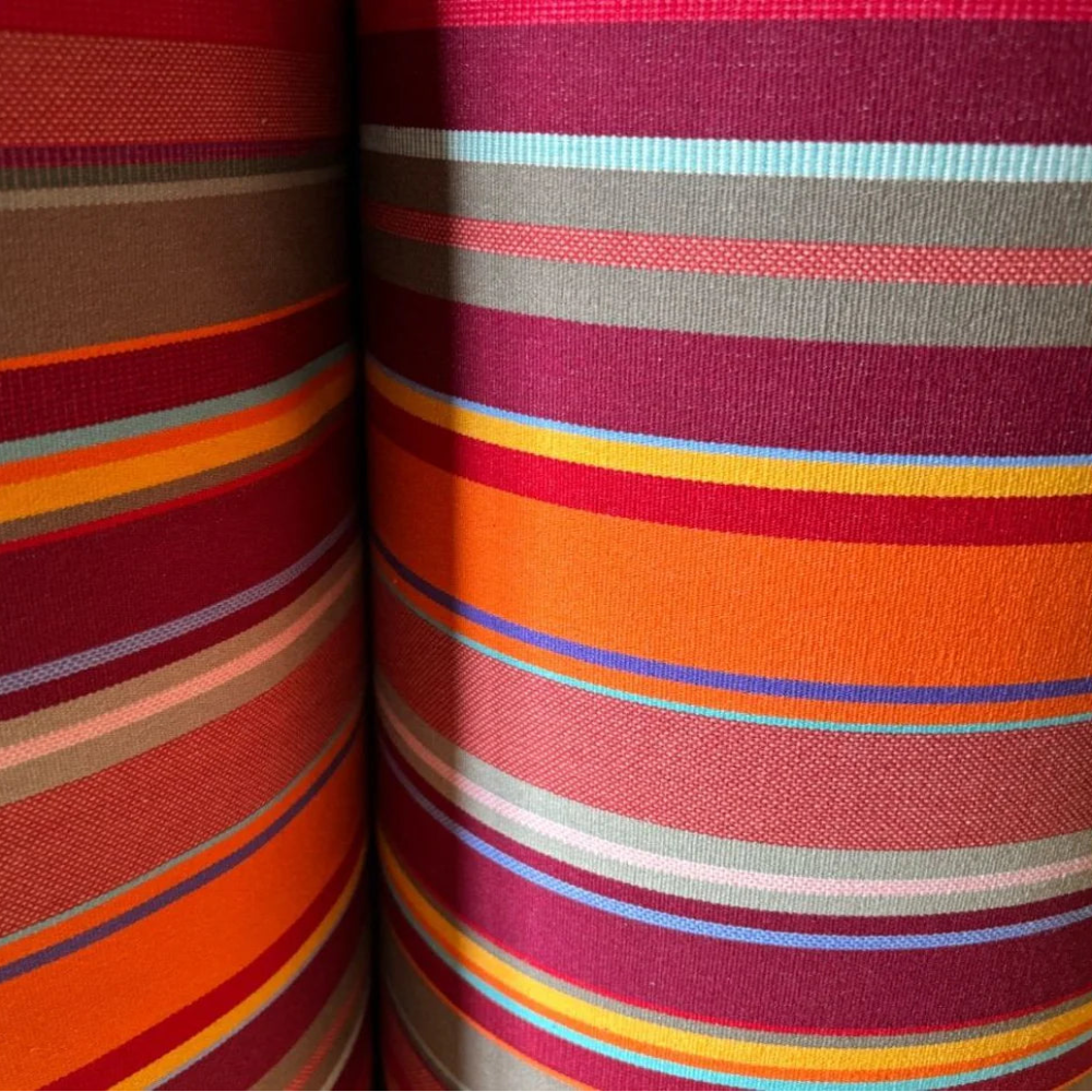 Close up of 43cm cotton Fabric in St Vincent Rouge, featuring a multicoloured striped pattern with various bands in reds, orange, purple, browns and different colours, indicating a vibrant and lively design. By Les Toiles du Soleil