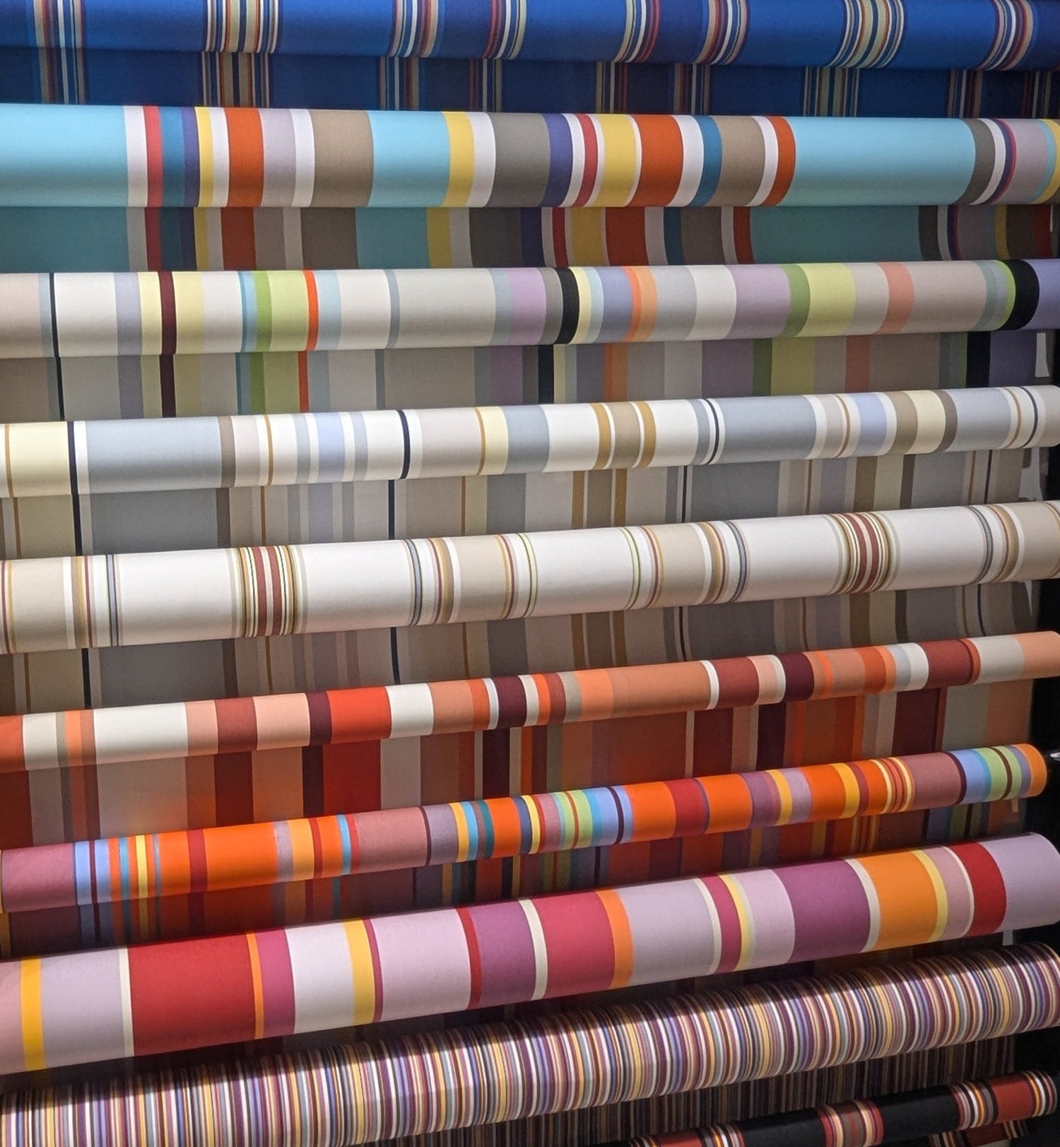 Rolls of colourful Sunbrella 174cm striped fabric on a rack.