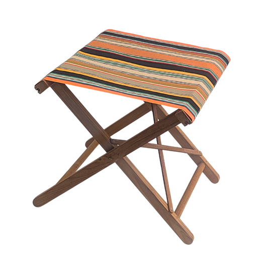 A Teak folding stool with a striped cotton Les Toiles du Soleil retro colours of orange, taupe, brown, and yellow. Shown on a plain white background.