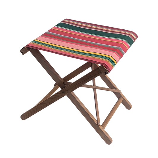 A teak folding stool  with Les Toiles du Soleil cotton fabric featuring stripes of red, crimson, candy pink, green, blue and golden yellow, inspired by the colours of the Catalan town of Toulouges and its famous onion.