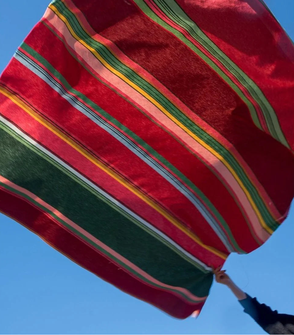 Lifestyle shot of Multi coloured striped fabric roll- Toulouges being thrown in the air. Fabric made up of light and darker shades of pink, purple and greens.