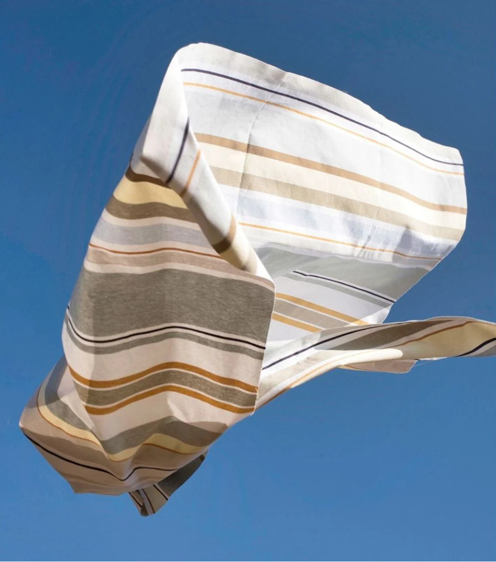 Les toiles du Soleil fabric thrown in the air. With a sky blue background the Trianon fabric reflects a delicate palette of soft greys, pale yellow, and sky blue, gently illuminated by touches of gold. 