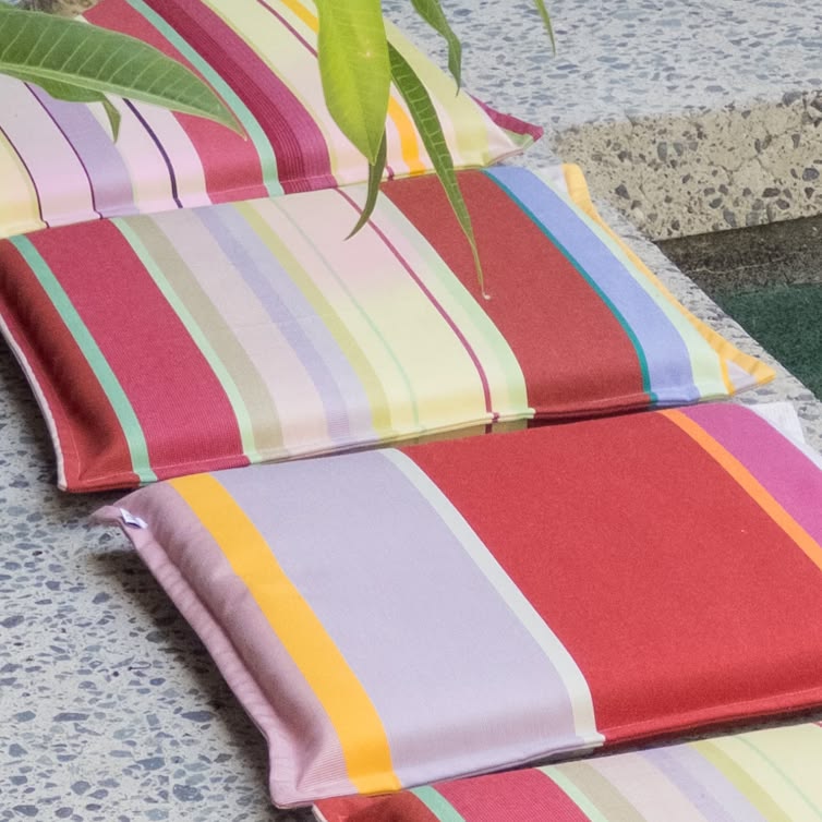 Placed next to a pool slim cushion made from Zinnia Les Toiles du Soleil Outdoor Sunbrella Fabric. Multi striped with rose, pinks, reds and yellows