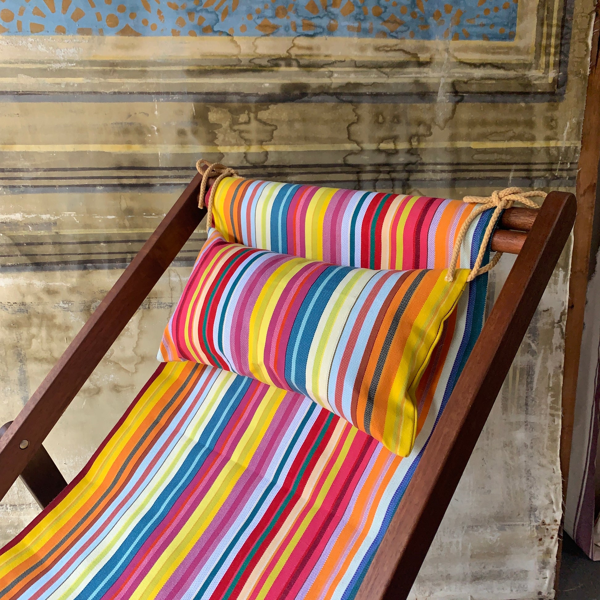 Wooden deckchair with head cushion in matching fabric. Featuring multicoloured stripes with detail